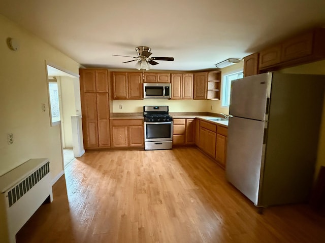 kitchen with light wood-style flooring, a sink, appliances with stainless steel finishes, radiator, and open shelves