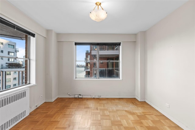 empty room featuring radiator, a healthy amount of sunlight, and baseboards