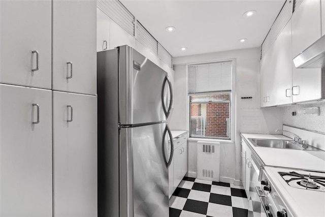 kitchen featuring freestanding refrigerator, a sink, light countertops, white gas range oven, and dark floors