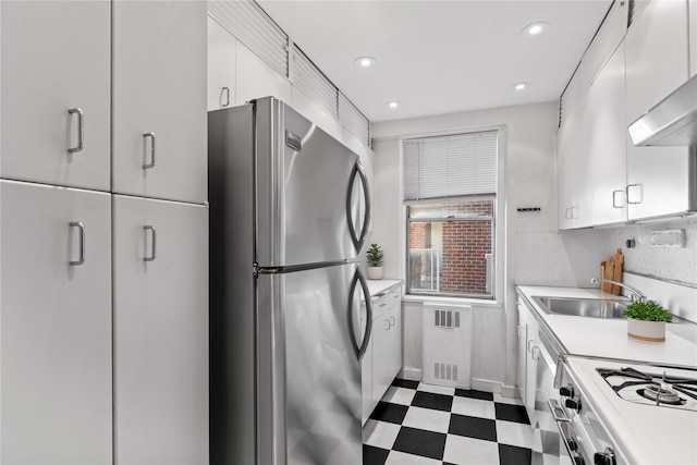 kitchen with white range with gas stovetop, freestanding refrigerator, a sink, light countertops, and dark floors