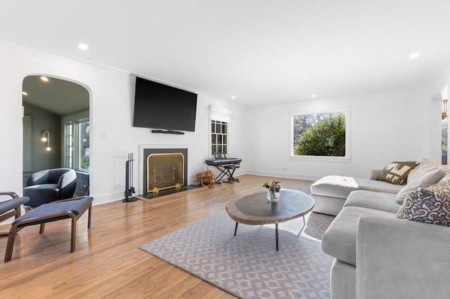 living area with baseboards, a fireplace with flush hearth, recessed lighting, arched walkways, and light wood-type flooring