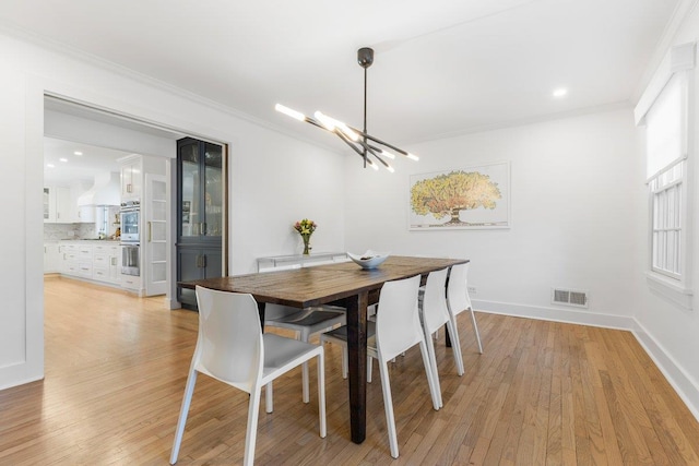 dining area featuring baseboards, visible vents, light wood-style floors, crown molding, and a chandelier