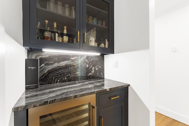 bar featuring tasteful backsplash, baseboards, beverage cooler, a dry bar, and light wood-style flooring