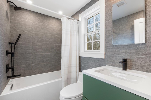 full bathroom with visible vents, toilet, shower / bath combo, tile walls, and vanity