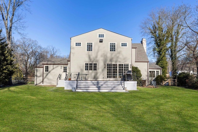 rear view of house with a yard, a deck, a chimney, and fence