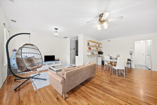 living area with light wood-style floors, ceiling fan, visible vents, and ornamental molding