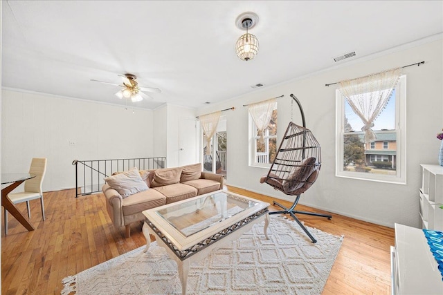 living room with a ceiling fan, light wood-type flooring, visible vents, and crown molding