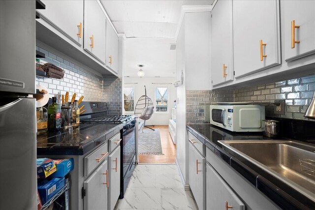 kitchen with white microwave, a sink, marble finish floor, gas stove, and dark countertops