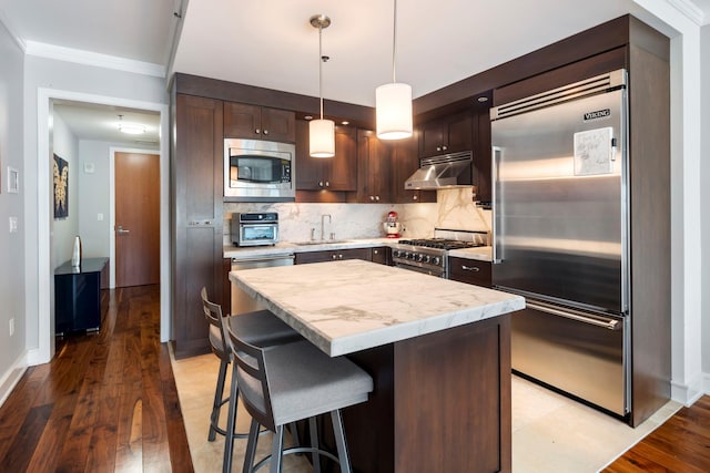 kitchen featuring built in appliances, backsplash, a sink, and under cabinet range hood