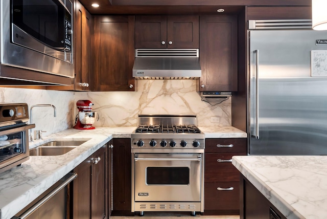 kitchen with dark brown cabinetry, high quality appliances, a sink, under cabinet range hood, and backsplash