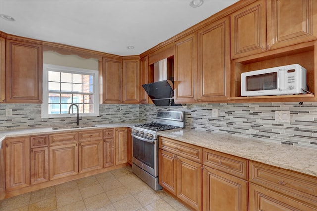 kitchen featuring white microwave, a sink, wall chimney exhaust hood, brown cabinetry, and stainless steel range with gas stovetop