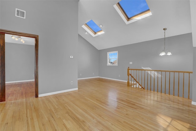 empty room with a skylight, light wood finished floors, visible vents, an inviting chandelier, and high vaulted ceiling