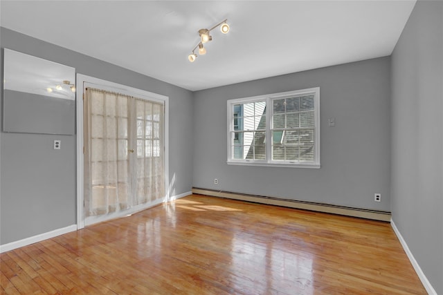 unfurnished room with baseboards, track lighting, a baseboard heating unit, and wood finished floors