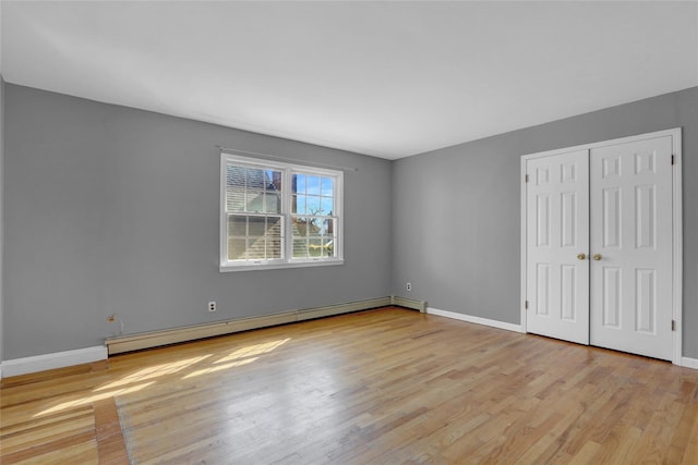 unfurnished bedroom with a closet, baseboard heating, wood finished floors, and baseboards