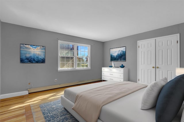 bedroom with baseboards, baseboard heating, a closet, and light wood-style floors