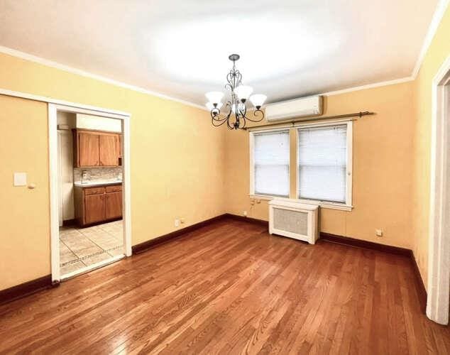 unfurnished room with radiator, light wood finished floors, a wall mounted air conditioner, crown molding, and a chandelier