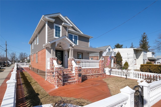 view of front of home with covered porch, a fenced front yard, and brick siding