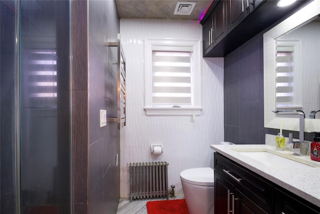 bathroom featuring radiator, tile walls, vanity, toilet, and visible vents