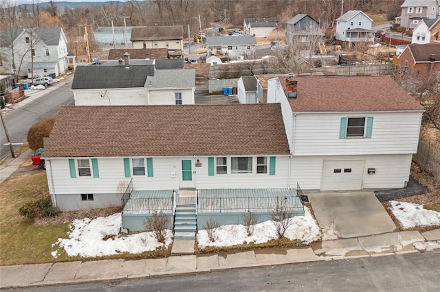 view of front of property featuring an attached garage, a residential view, concrete driveway, and roof with shingles