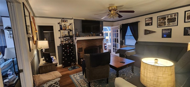 living room with crown molding, a fireplace, ceiling fan, and wood finished floors