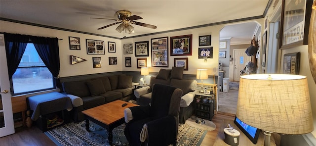 living room featuring arched walkways, a wainscoted wall, wood finished floors, a ceiling fan, and crown molding