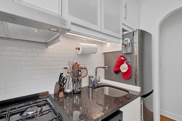 kitchen with stovetop, arched walkways, a sink, decorative backsplash, and under cabinet range hood