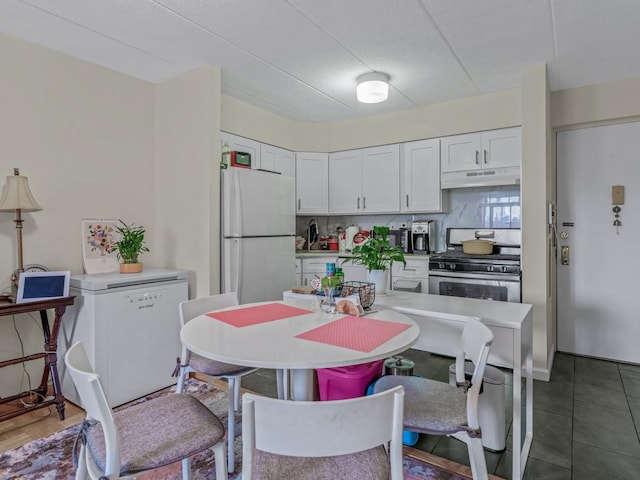 kitchen with refrigerator, freestanding refrigerator, stainless steel range with gas stovetop, white cabinetry, and under cabinet range hood