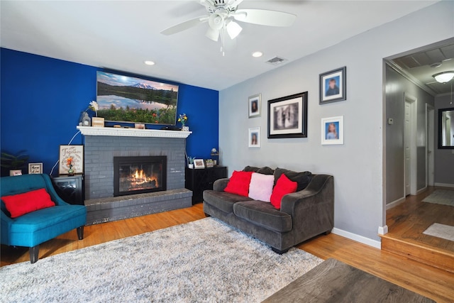 living area featuring a fireplace, wood finished floors, a ceiling fan, visible vents, and baseboards