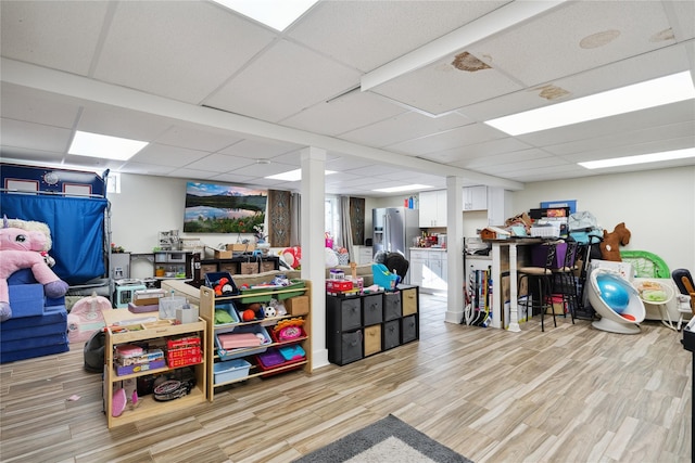 finished below grade area with a paneled ceiling, stainless steel fridge, and light wood-style flooring