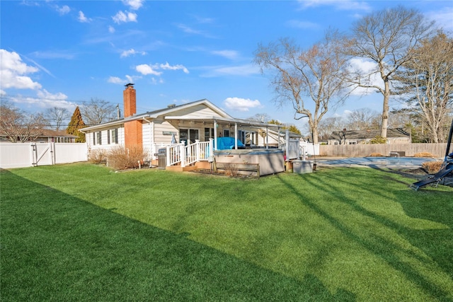 back of property featuring a hot tub, a covered pool, a fenced backyard, a chimney, and a yard