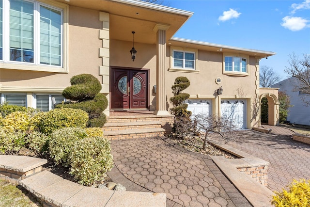 entrance to property with a garage, decorative driveway, and stucco siding