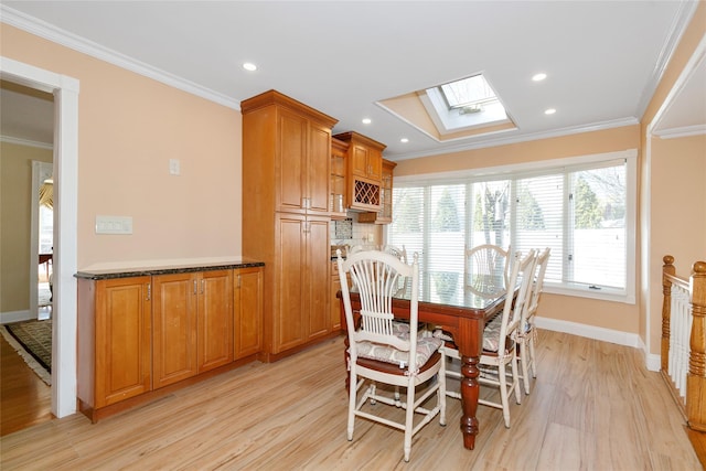 dining space with a skylight, baseboards, light wood-style floors, and crown molding