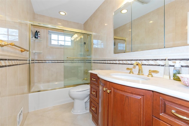 bathroom with toilet, shower / bath combination with glass door, tile patterned flooring, vanity, and tile walls