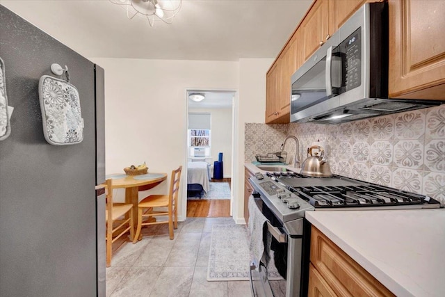 kitchen with light countertops, decorative backsplash, appliances with stainless steel finishes, a sink, and baseboards