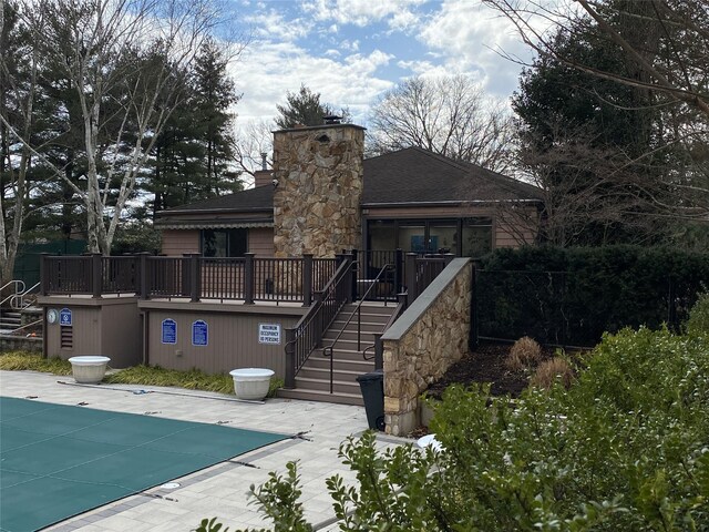 rear view of property with a patio, a chimney, stairway, a community pool, and a wooden deck