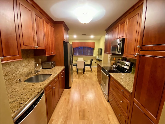 kitchen featuring light stone counters, stainless steel appliances, backsplash, a sink, and light wood-type flooring