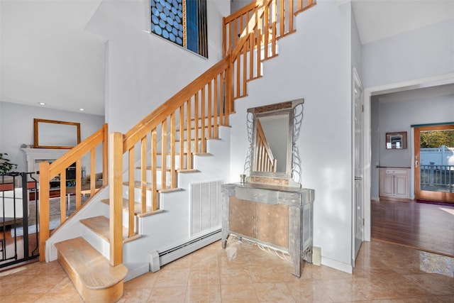 stairs with visible vents, a towering ceiling, a baseboard heating unit, baseboards, and tile patterned floors