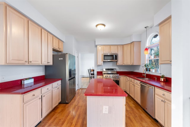 kitchen with a center island, light wood finished floors, dark countertops, appliances with stainless steel finishes, and a sink