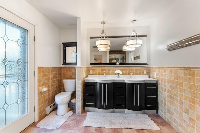 bathroom featuring tile walls, double vanity, toilet, a baseboard heating unit, and a sink