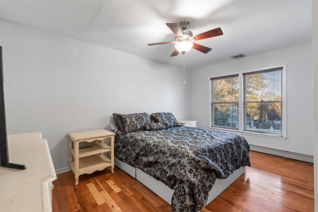 bedroom featuring hardwood / wood-style flooring, visible vents, a baseboard heating unit, and a ceiling fan