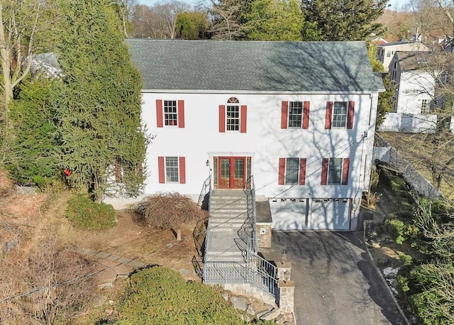 colonial house featuring a garage, driveway, roof with shingles, and french doors