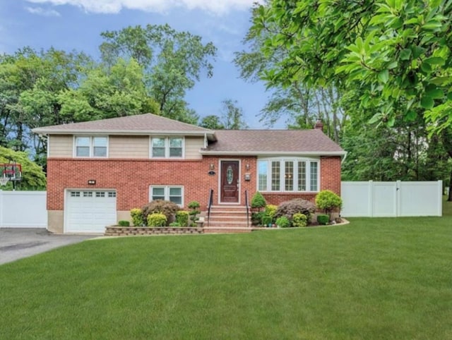 tri-level home with a chimney, aphalt driveway, fence, a front yard, and brick siding