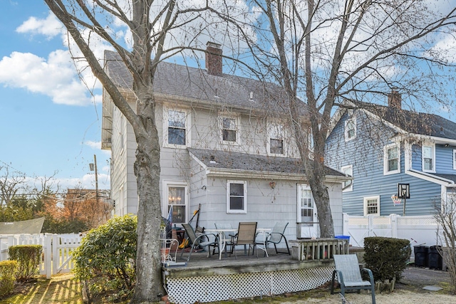 back of house with a shingled roof, a chimney, fence, and a deck