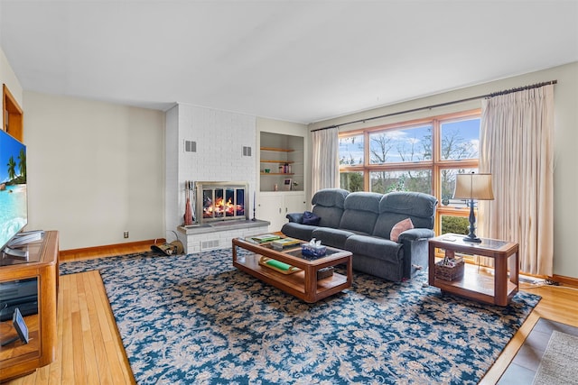 living area featuring built in features, baseboards, visible vents, and wood finished floors