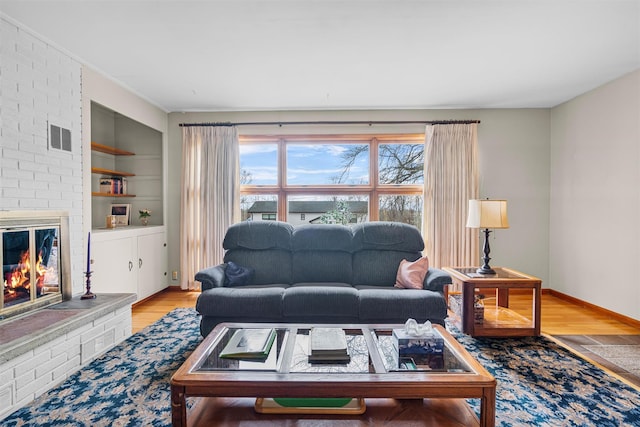 living room featuring built in shelves, visible vents, a fireplace, and wood finished floors