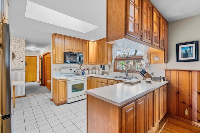 kitchen featuring a skylight, gas range gas stove, light countertops, a sink, and black microwave