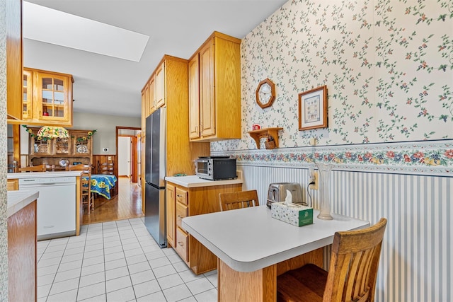 kitchen featuring wallpapered walls, light countertops, dishwasher, and wainscoting