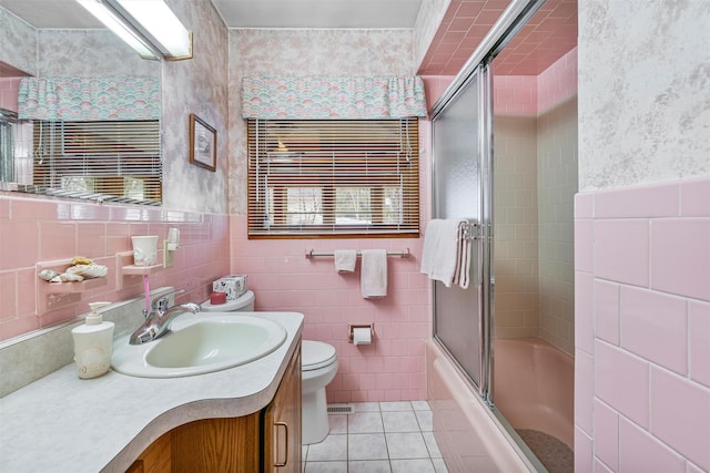 bathroom with tile walls, toilet, combined bath / shower with glass door, vanity, and tile patterned flooring