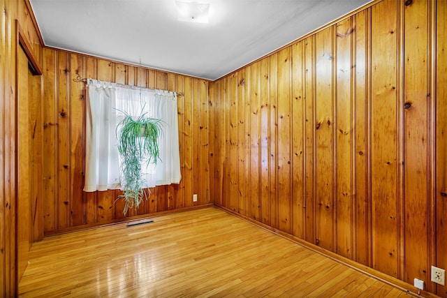 empty room with wood walls, wood-type flooring, visible vents, and baseboards