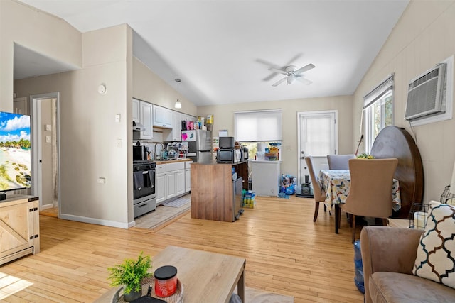 living area with light wood-style flooring, a ceiling fan, a wall mounted AC, baseboards, and vaulted ceiling